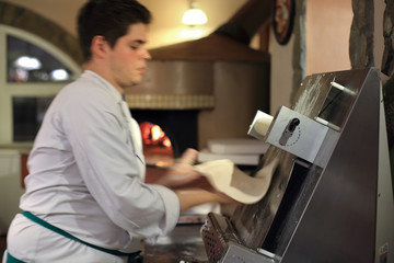 Piekarz wałkuje ciasto na pizzę w maszynie. - obrazy, fototapety, plakaty