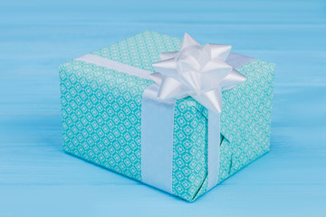 Green patterned gift box with white ribbon. Blue wooden table background.