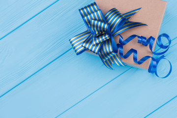 Brown cardboard box with blue ribbon bow. Blue wood background.