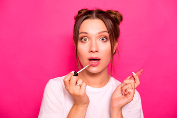 Sexy woman with stylish hairstyle in white t-shirt on a pink background applying make up, making amazed emotions