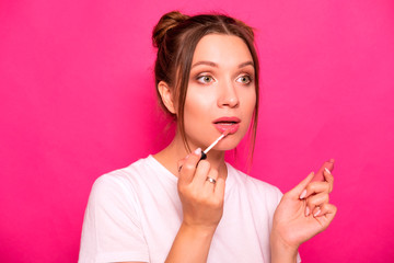 Sexy woman with stylish hairstyle in white t-shirt on a pink background applying make up, making amazed emotions