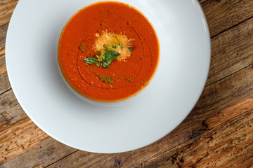 Vegetable tomato soup with cheese and green herbs on rustic wooden background. Top view