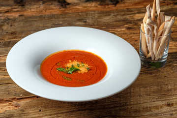 Vegetable tomato soup with cheese and green herbs. Glass of grissini