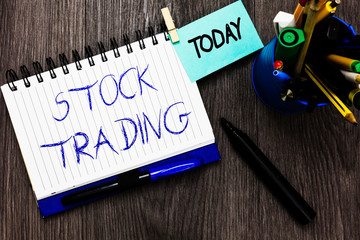 Handwriting text Stock Trading. Concept meaning Buy and Sell of Securities Electronically on the Exchange Floor Open notebook clothespin holding reminder cup markers wooden background