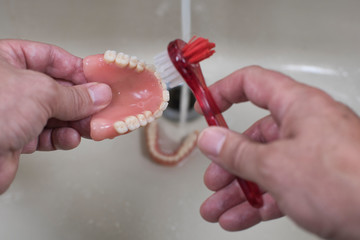 denture cleaning with brush / denture cleaning with brush in the sink with running water
