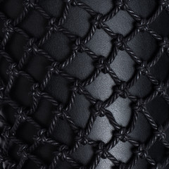 Luxury black leather covered with black rope net. Beautiful background. Closeup.