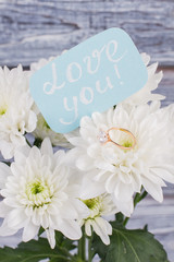 Wedding ring on white bouquet of flowers. Romantic gift for Valentines holiday. Marriage proposal ideas.