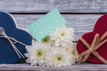 Romantic composition for Valentines Day. Red and blue heart-shaped gift boxes and bouquet of white flowers on wooden background. Saint Valentines Day concept.