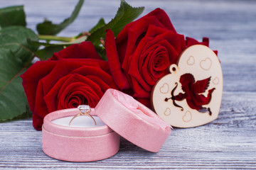 Engagement ring in box and flowers. Red roses, wooden heart and diamond ring. Valentines Day concept. Perfect gift for romantic day.