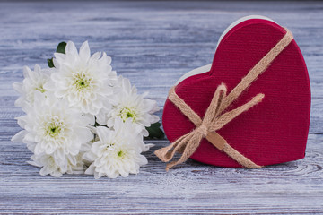 Red heart-shaped gift box and white flowers. Bunch of chrysanthemum flowers and red box in a shape of heart on wooden background. Happy Valentines Day.