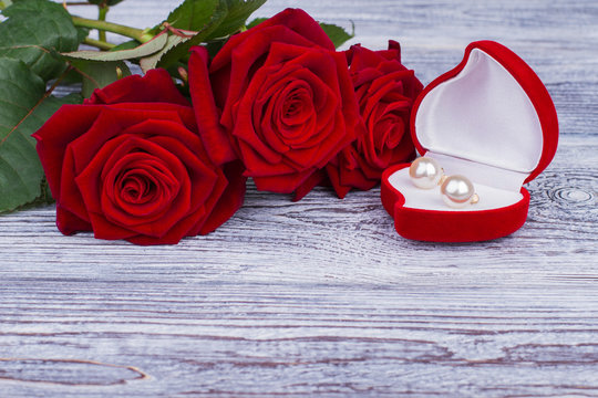 Roses, golden accessory and copy space. Velvet heart shaped box with pearl earrings and fresh flowers on wooden background. Valentines Day greeting background.