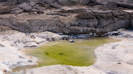 a small greenish lake and salt deposit at a rocky volcanic coast