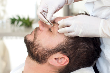 Kosmetyczka podczas zabiegu regulacji brwi u mężczyzny. Wyrywanie zbędnych włosów na brwiach - obrazy, fototapety, plakaty