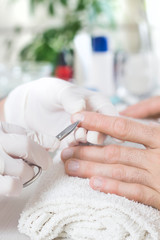 Mężczyzna w salonie kosmetycznym podczas zabiegu manicure. Wycinanie skórek na dłoni przy paznokciu za pomocą nożyczek. - obrazy, fototapety, plakaty