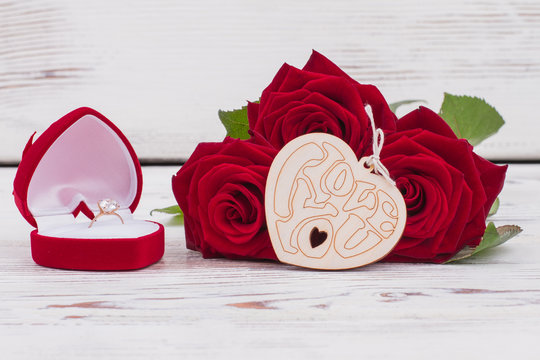 Roses, golden ring and wooden heart. Valentines Day background with red flowers and engagement ring in box. Happy Valentines Day.