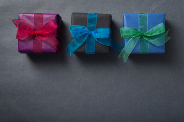 Wrapped presents with colorful ribbons over dark grey background, top view