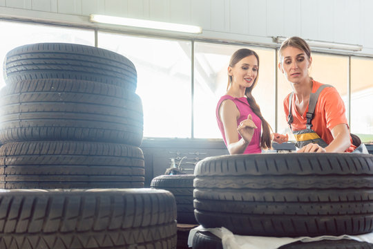 Helpful experienced female auto mechanic checking the identification number of a tire for a customer in an automobile repair shop with various tires for sale