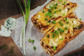 Baked open faced cheese sandwiches with mozzarella, gorgonzola and green onion on a rustic wooden table.