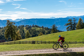 E-Mountainbikerin fährt über Wiesen und Feldern mit Blick in die Berge