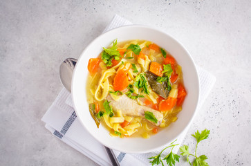 Chicken noodle soup and vegetables in a white bowl on a white background.