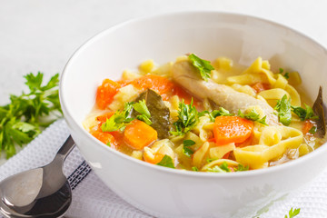 Chicken noodle soup and vegetables in a white bowl on a white background, copy space.