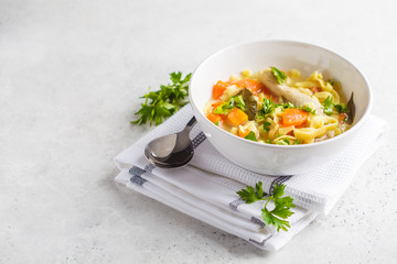 Chicken noodle soup and vegetables in a white bowl on a white background, copy space.