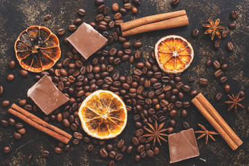 Coffee grains, orange slices, chocolate and cinnamon sticks and star anise on a dark background....