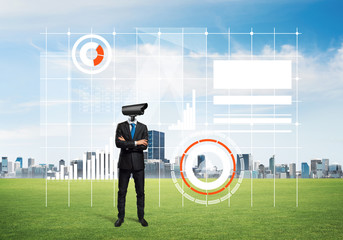 Camera headed man standing on green grass against modern cityscape