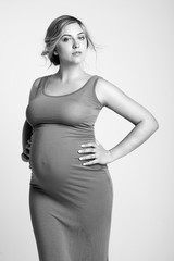 A beautiful pregnant woman with blond hair in a tight knitted dress. Black and white photo.