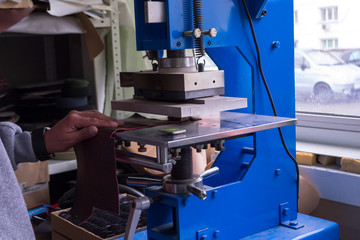 The man in the workshop presses the lever on the press machine to get the embossed logo and letters on the leather product that heats the cliche and squeezes the desired image on the material