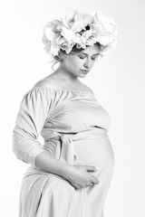 Beautiful pregnant woman in dress and flower wreath. On a white background. Black and white photo in bright tonality.