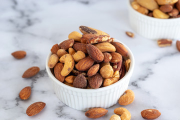 roasted mixed nuts in white ceramic bowl on barble table background.