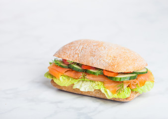 Fresh healthy salmon sandwich with lettuce and cucumber on white stone background. Breakfast snack. Space for text