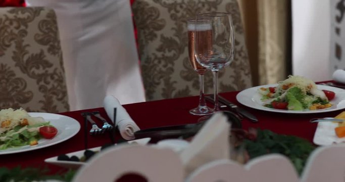 Slow motion of table in luxury restaurant preparing for dinner with best dishes. Close up of tasty classic salad cezar with tomato, chicken, mozzarella cheese on white rounded plate. Food concept.