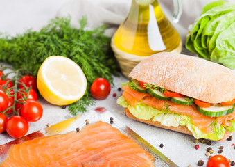 Fresh healthy salmon sandwich with lettuce and cucumber on the plate on white stone background. Breakfast snack. Fresh tomatoes, dill and lemon. Tray of salmon