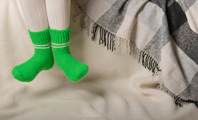 Female legs in warm white knitted tights and green socks on a white background made of faux fur