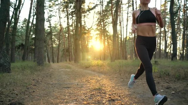 Close up of woman with headphones running through an autumn forest at sunset