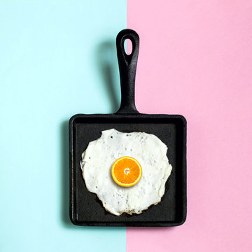 Cast-iron frying pan with fried eggs, half of orange instead of yolk