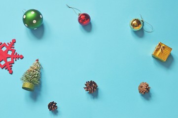 Flat lay Christmas photography. Snowflake, colorful balls, golden gift box, decorative fir tree and pine cones on a blue background. New Year home decoration