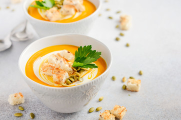 Pumpkin soup with cream, croutons, pumpkin seeds and parsley on a gray concrete or stone background, selective focus, copy space
