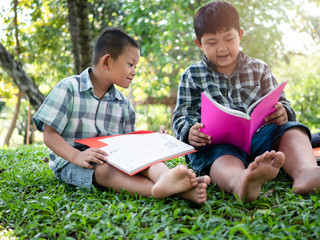 Fototapeta premium Cute two asian student boy reading book in the nature park with sunlight background, people, learning, relax, education and Natural classroom concept..