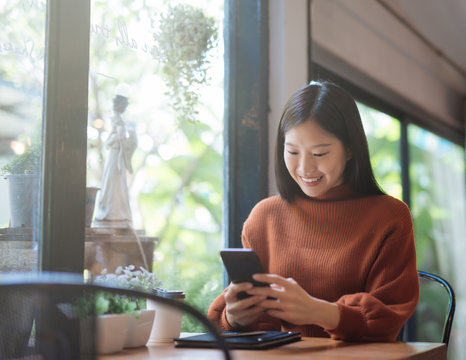 Young Asian woman using phone at a coffee shop happy and smile.