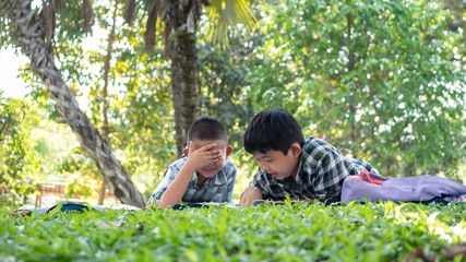 Fototapeta premium Cute two asian student boy reading book in the nature park with sunlight background, people, learning, relax, education and Natural classroom concept..