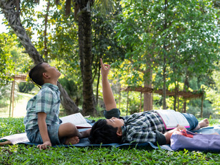 Naklejka na ściany i meble Cute two asian student boy reading book in the nature park with sunlight background, people, learning, relax, education and Natural classroom concept..