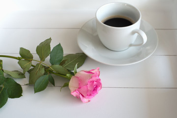 Schwarzer Kaffee in weißer Tasse mit Untertasse neben rosafarbener Rose auf weißem Tablett