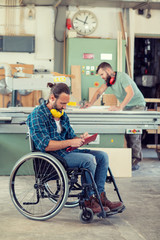 worker in wheelchair in a carpenter's workshop with his colleagu