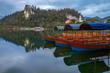Naklejka premium Tourist boats on the on Lake Bled. Beautiful mountain lake Bled and Medieval castle on the rock. Scenery at Bled lake in Slovenia. Mountains in background. Slovenia, Europe. European travel.