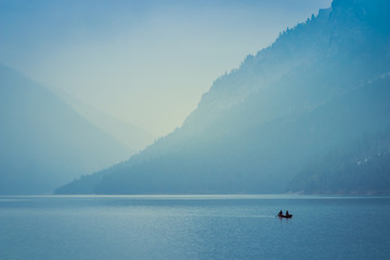 Two people rowing a small boat on lake Plansee in the European Alps, in Austria at early morning sunrise