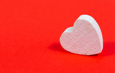 Fototapeta premium Small wooden white heart in front of red background