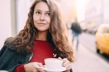  Young beautiful woman drinking coffee in a cool sunny morning in the city. long-haired fashion girl.